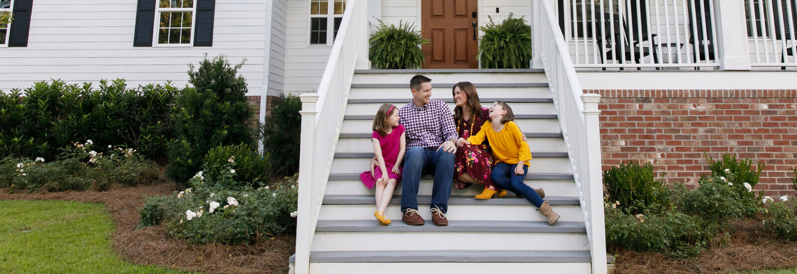 A young family sitting on the front stairs of a large home